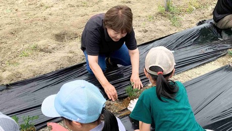 子どもたちに野菜の苗の植え方を教える安岡理事長 (写真：ことのは舎)